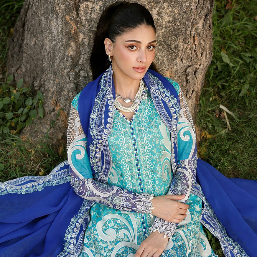 Woman in a blue and white embroidered traditional outfit sitting against a tree.